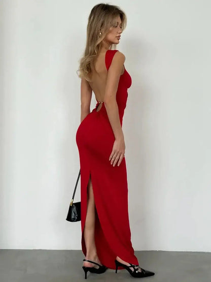 Back view of a woman in a red maxi dress with a sleek design and side slit, showcasing gold ring details and elegant silhouette.