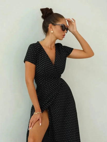Model wearing a black polka dot maxi dress with a wrap silhouette and thigh-high slit, styled for elegance.