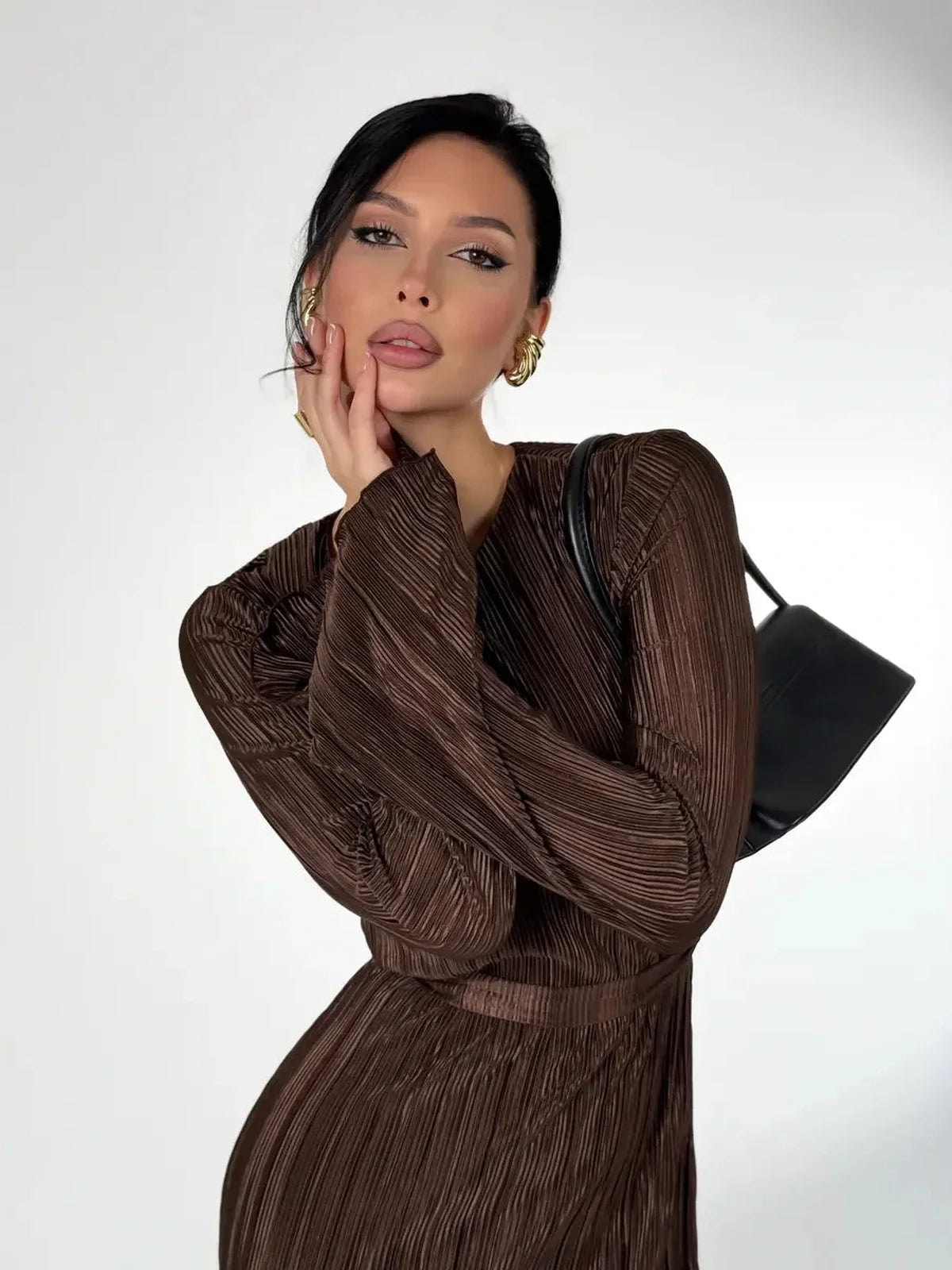 Model elegantly posing in a Mocha Drape Maxi Dress with pleats and a black handbag, showcasing a stylish minimalist look.