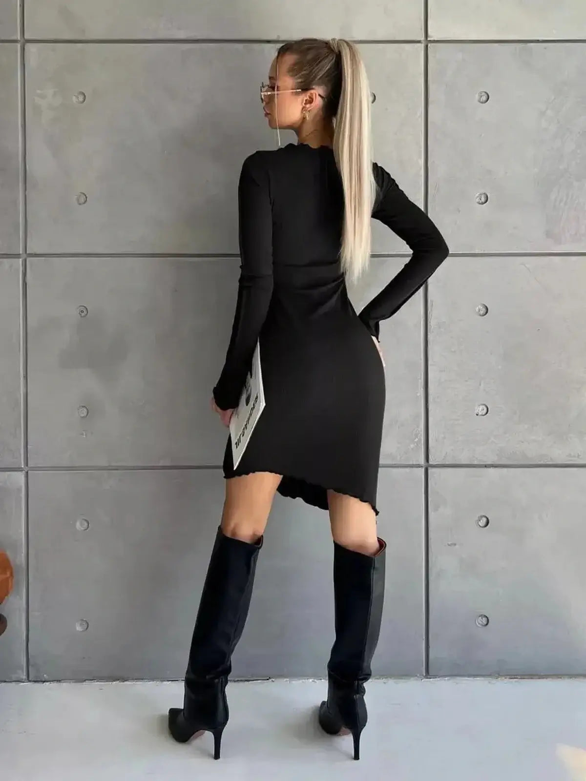 Black long sleeve mini dress with a high-low hem and knee-high boots, showcasing a modern edgy style.