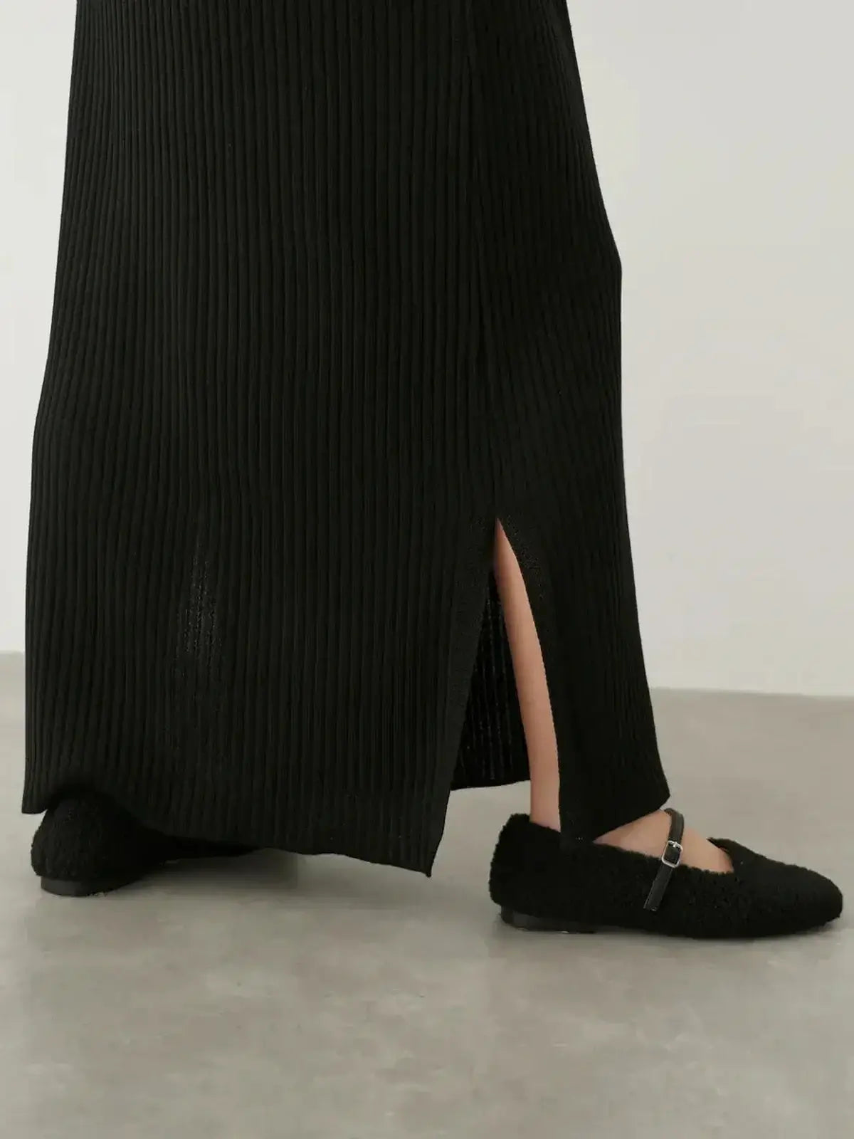 Detail of the Muse Knit Maxi Dress showcasing a subtle side slit, paired with stylish black shoes on a neutral backdrop.