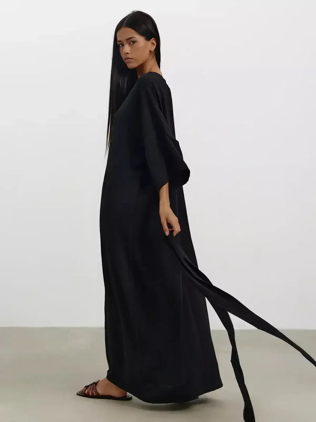 Elegant woman in a black Noir Drift Maxi Dress with kimono sleeves and soft sculpted belt, showcasing a fluid silhouette.