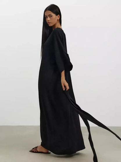 Elegant woman in a black Noir Drift Maxi Dress with kimono sleeves and soft sculpted belt, showcasing a fluid silhouette.