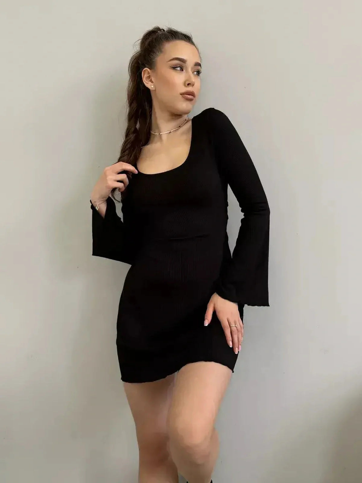 Model showcasing the Noir Flare black mini dress with flared sleeves and a deep square neckline.