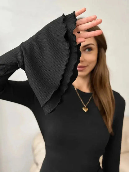 Close-up of a woman's hand with ruffled sleeves of a black mini dress, showcasing its elegant design.