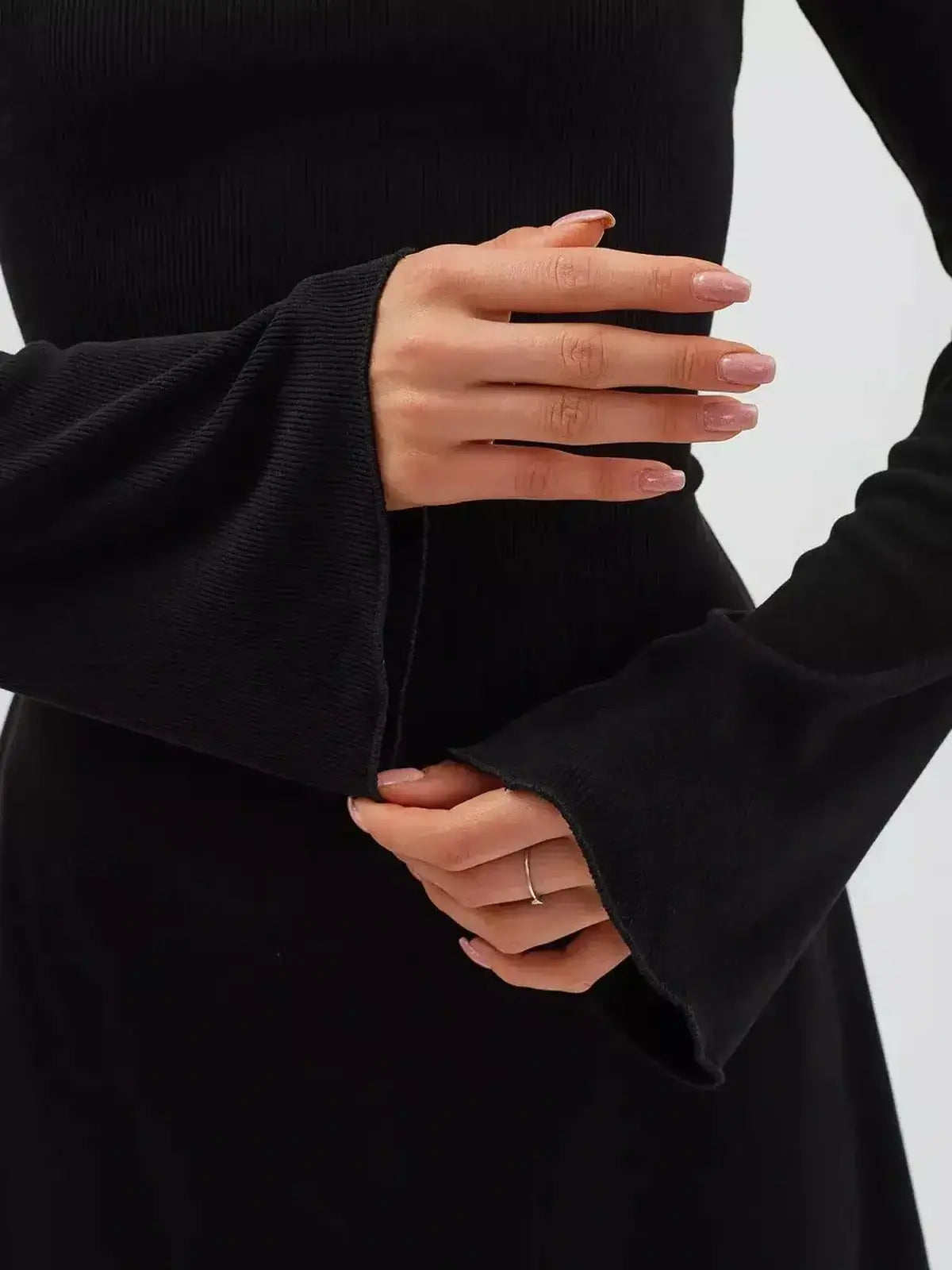 Close-up of a woman's hands in a black flare mini dress, showcasing long flared sleeves and a cinched waist.