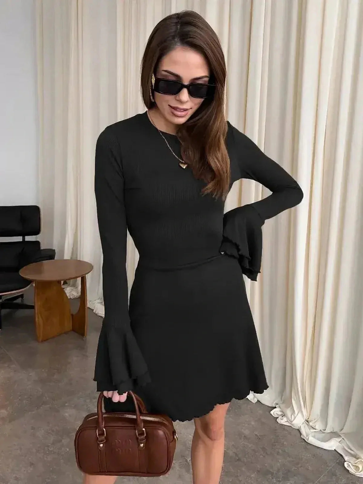 Model wearing a chic Noir Flare Mini black dress with flared cuffs and a tie waist, styled for modern elegance.
