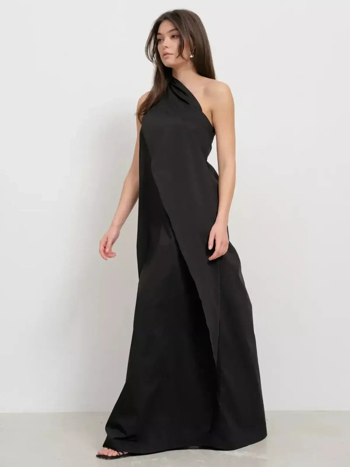 Black one-shoulder maxi dress showcasing draped elegance and a sculptural silhouette.