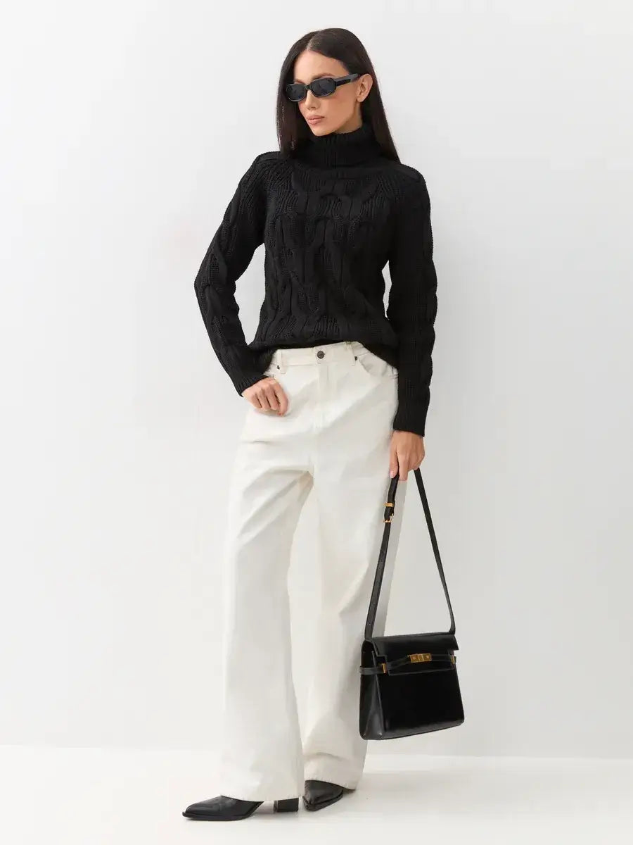 Noir Knitwear by Lauven: Woman in black cable-knit turtleneck sweater, white pants, and stylish bag.