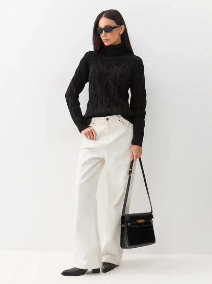 Noir Knitwear by Lauven: Woman in black cable-knit turtleneck sweater, white pants, and stylish bag.