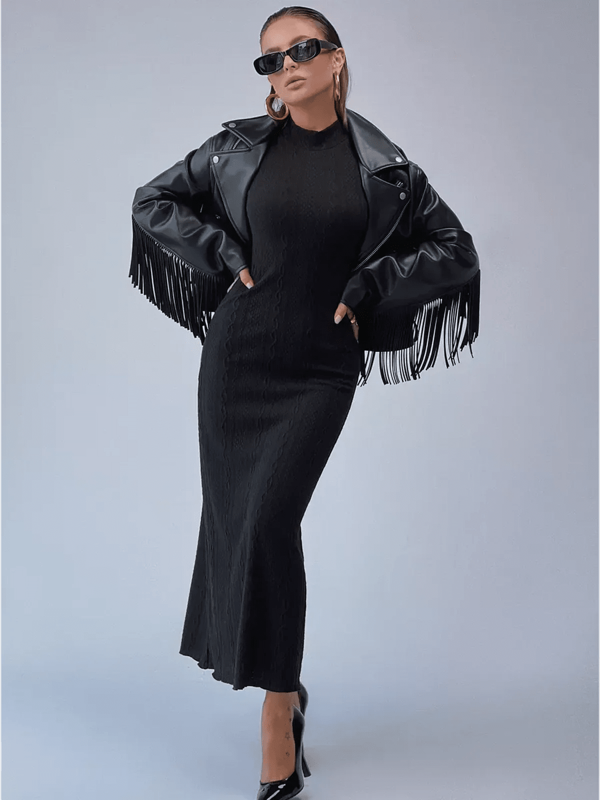 Woman in a sleek Noir Sculpt Maxi Dress with a trendy fringed leather jacket and sunglasses, exuding modern elegance.