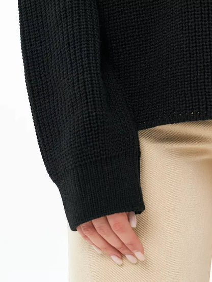 Close-up of hand wearing the Noir Sweater by Lauven, showcasing the textured knit and oversized fit in classic black.