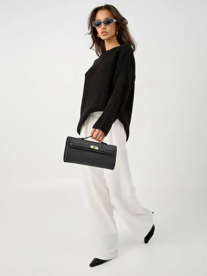 Model wearing Nola Sweater, oversized black knit, with stylish sunglasses and white pants, carrying a black handbag.