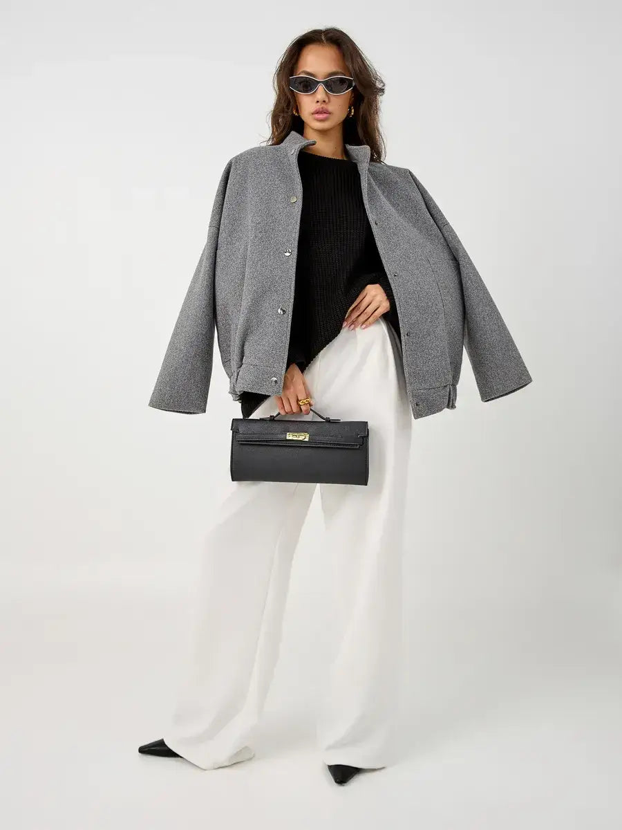 Model wearing Nola Sweater by Lauven, styled with a gray jacket and white pants, holding a black handbag.