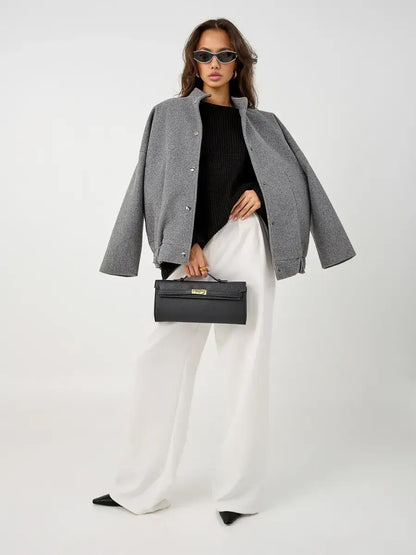 Model wearing Nola Sweater by Lauven, styled with a gray jacket and white pants, holding a black handbag.