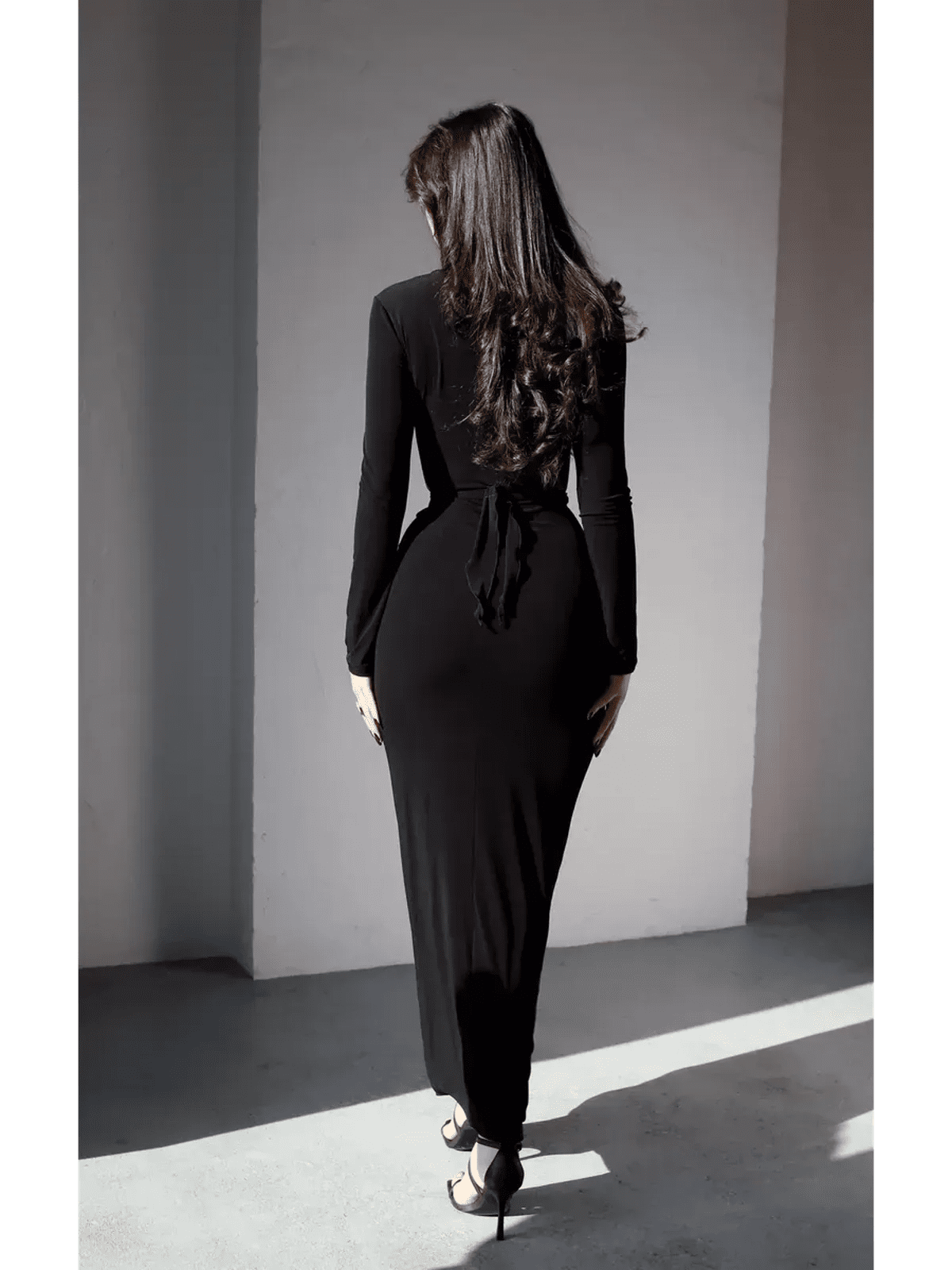 Back view of a woman in a sleek black Obsidian Drape Maxi Dress, showcasing its elegant silhouette and tie detail.