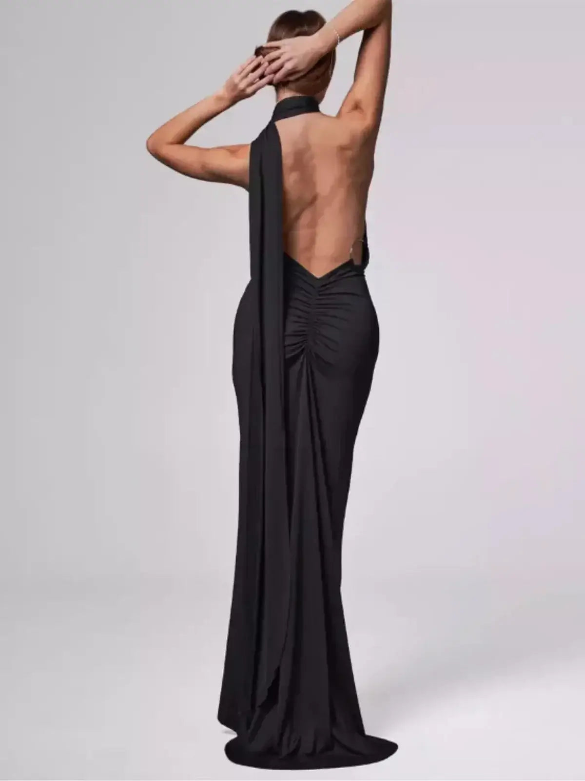 Back view of a woman in a sleek black Obsidian Maxi Dress showcasing an elegant asymmetrical design.