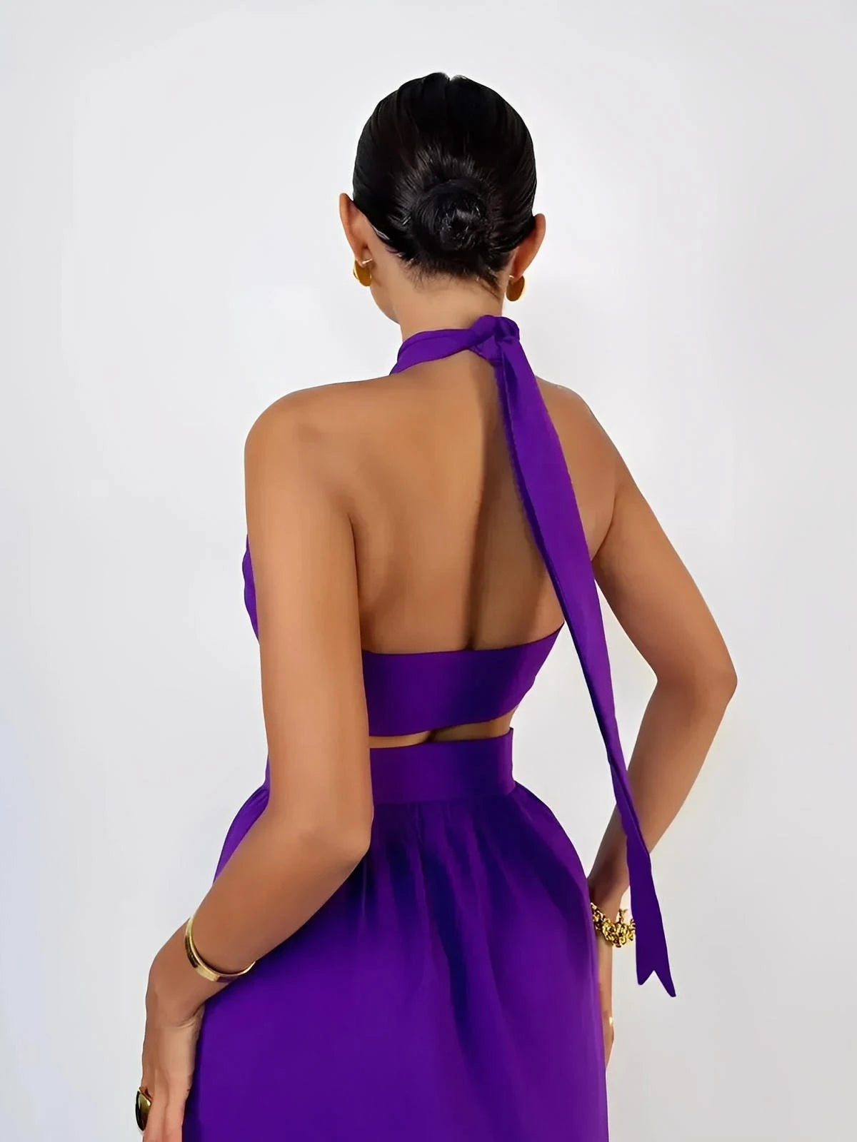 Back view of a woman in a vibrant orchid purple halter top and high-waisted maxi skirt, showcasing a bare back and elegant tie detail.
