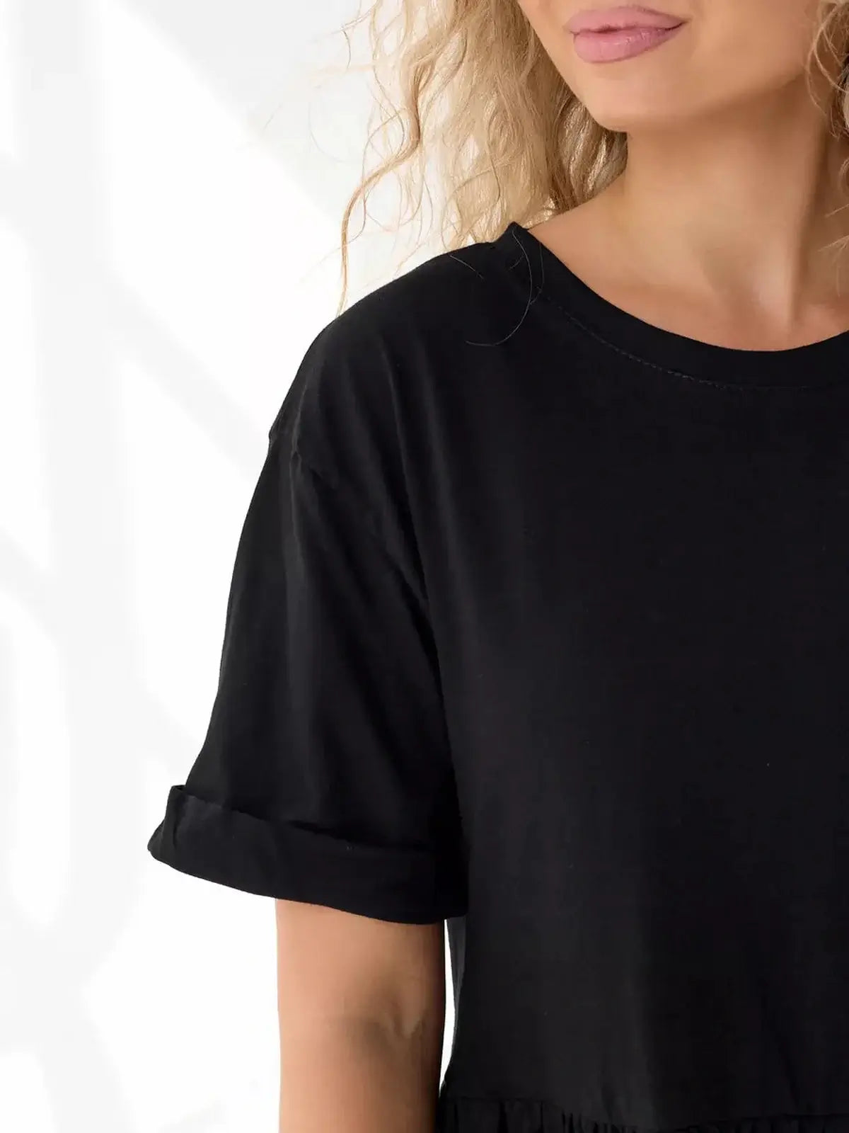 Close-up of the tiered black mini dress showcasing its relaxed fit and rolled short sleeves, perfect for summer.