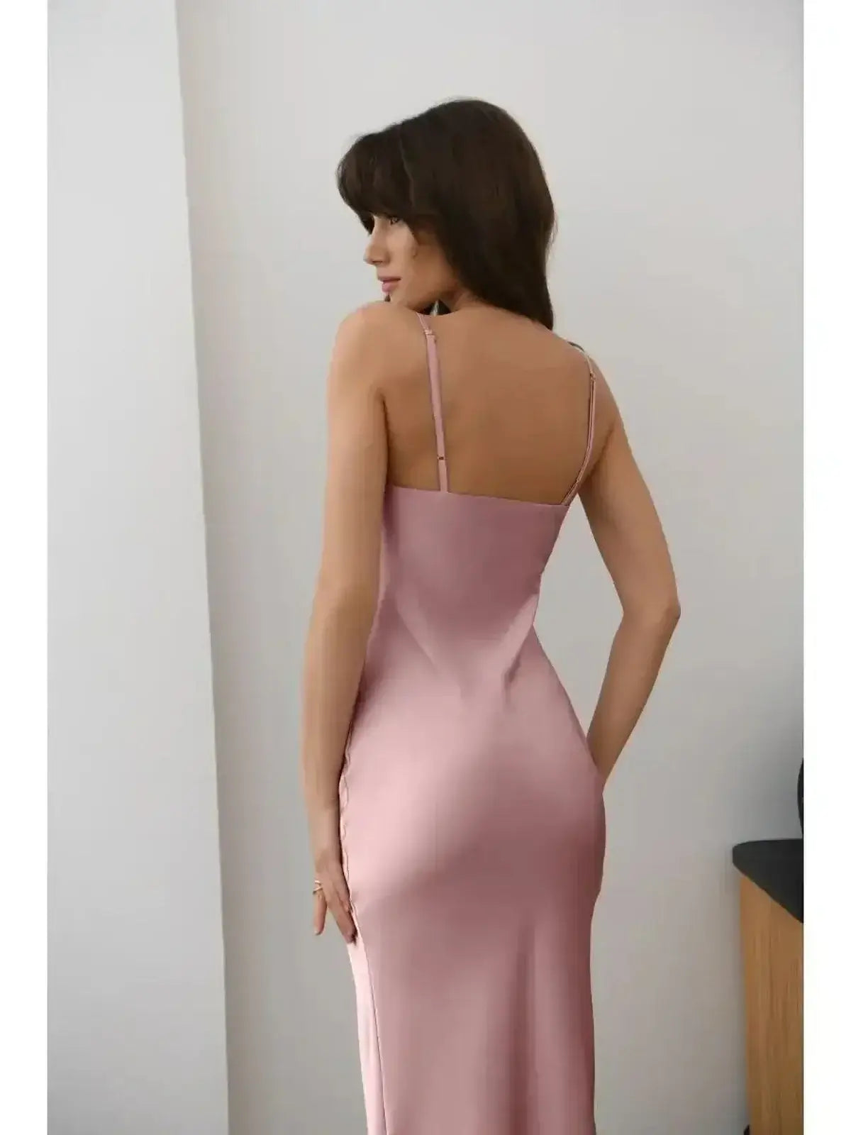 Back view of a woman in a muted rose satin midi dress showcasing its sleek silhouette and luxurious drape.