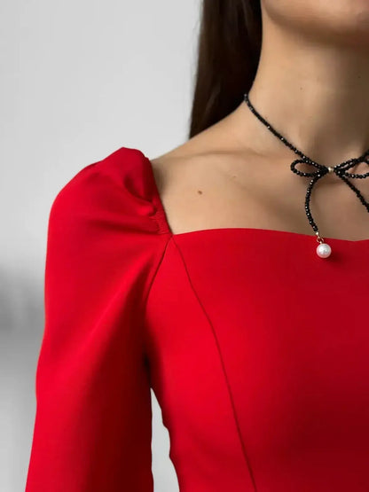 Close-up of a woman's shoulder in a stylish red mini dress, showcasing a square neckline and elegant puff sleeves.