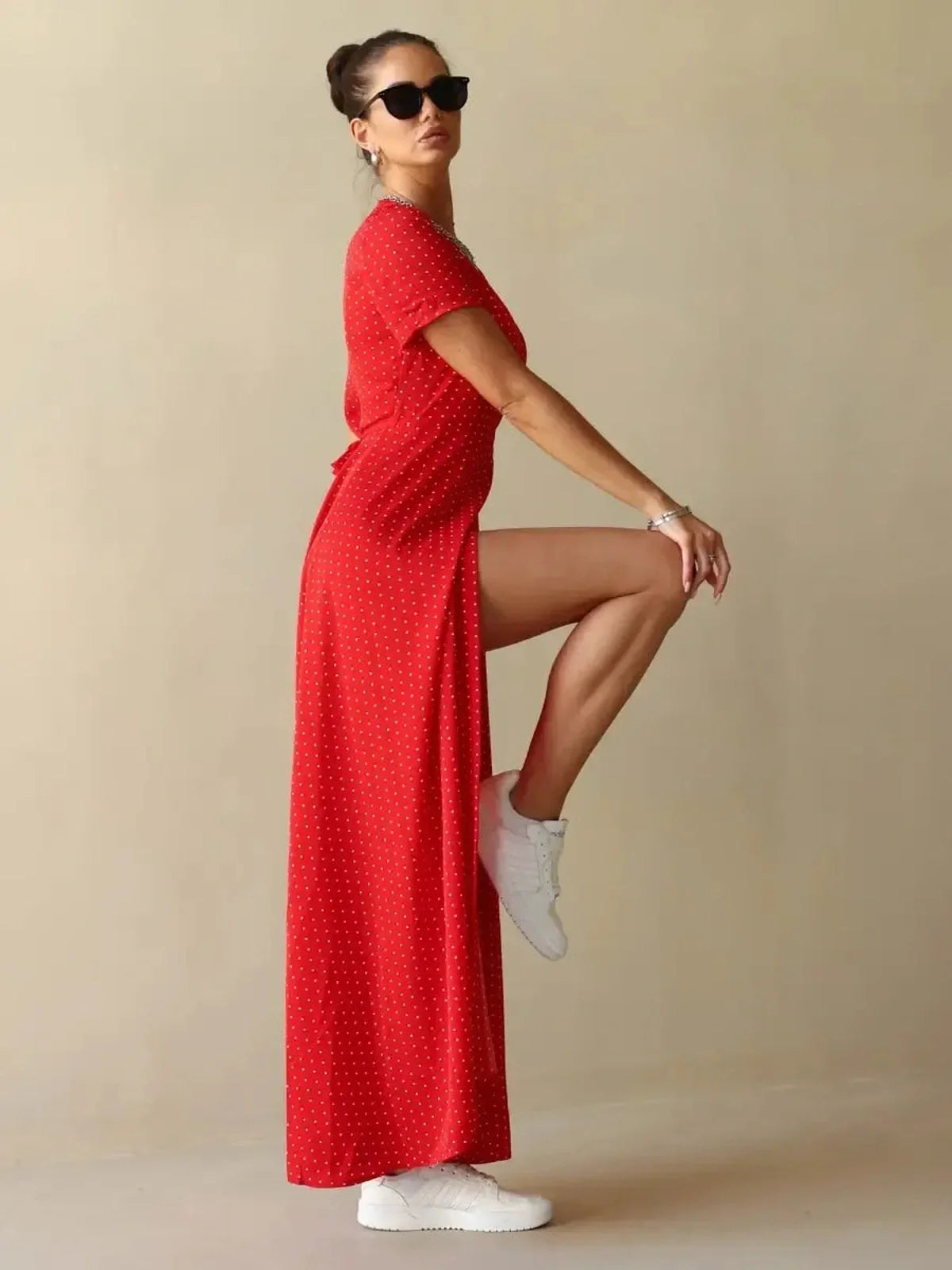 Model wearing Ruby Grace Maxi Dress in red polka dots with side slit, styled casually with white sneakers.
