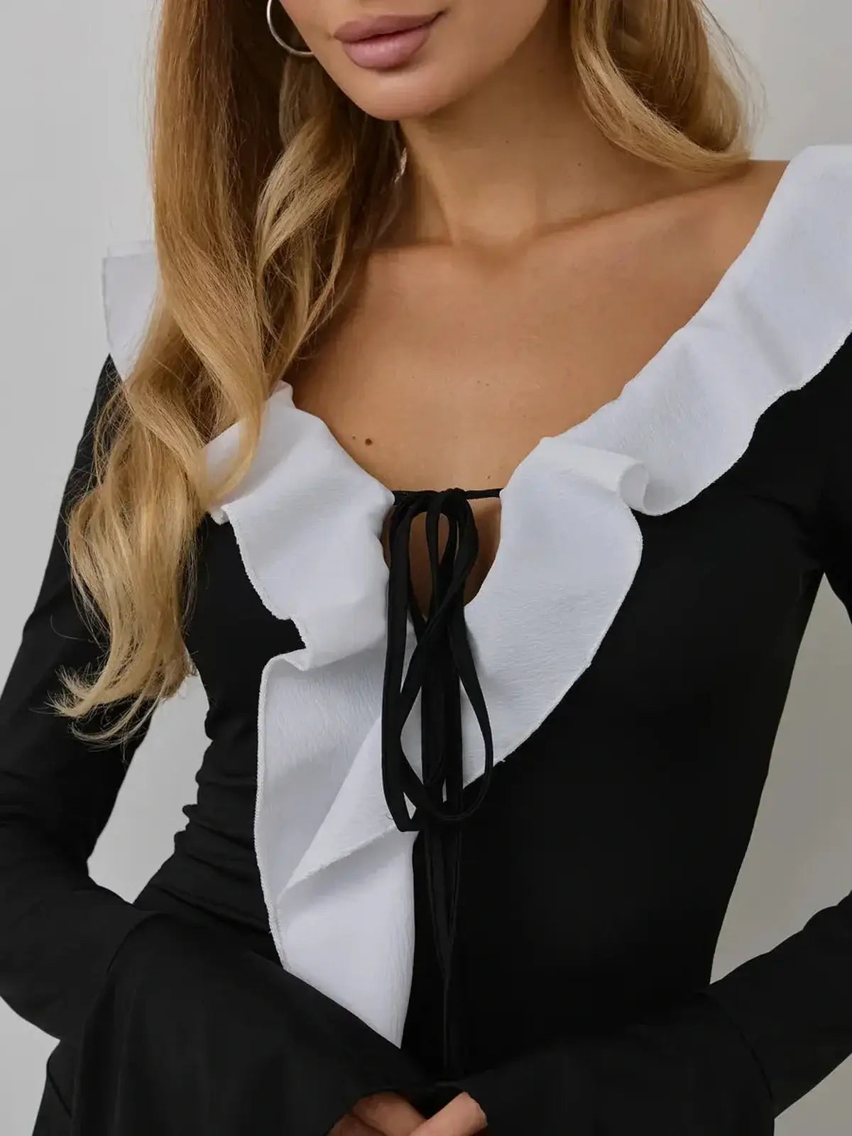 Close-up of a model wearing the Ruffle Affair mini dress with a crisscross neckline and sculptural white ruffle.