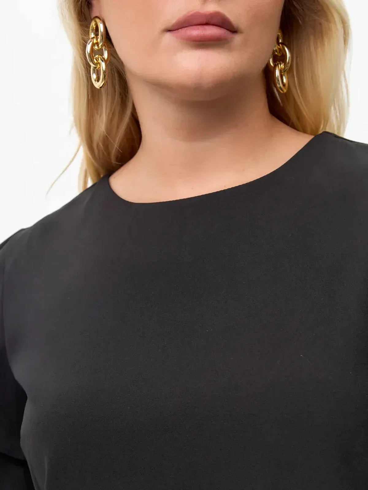 Close-up of a woman wearing a black dress with ruffle details, showcasing elegant earrings and a stylish neckline.