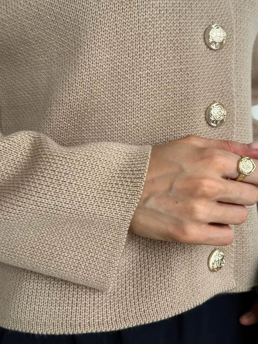 Close-up of a hand wearing a ring and buttoned Sable Cardigan by Lauven in elegant beige knit.
