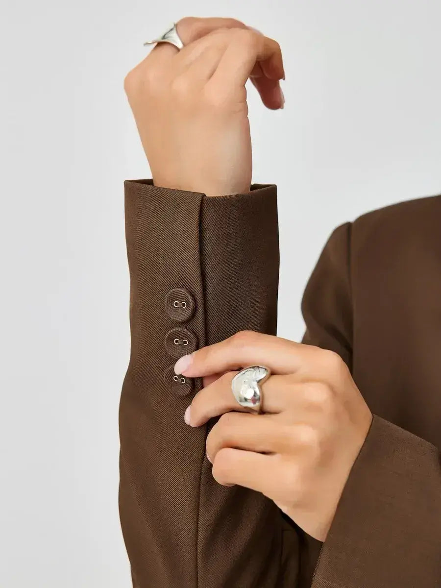 Close-up of a woman's hand fastening button on a brown sleeve of the Saffron Blazer by Lauven.