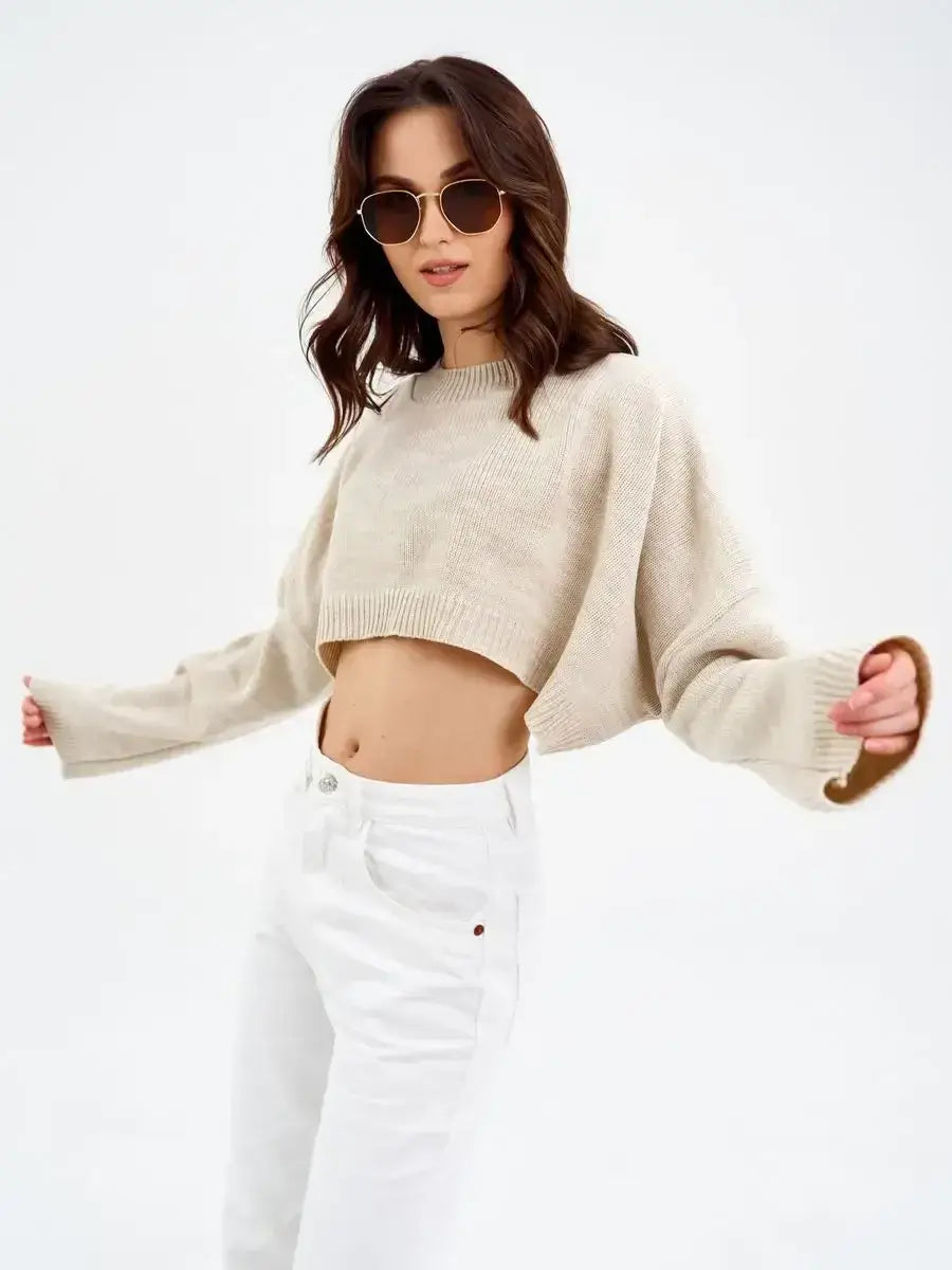 Stylish model wearing a cropped oversized knit Sand Sweater by Lauven in light beige, paired with white pants.
