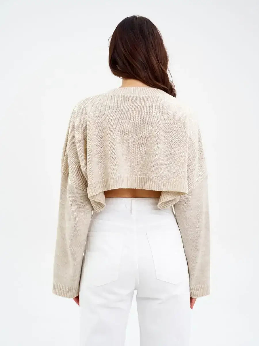 Back view of the Lauven Sand Sweater, a cropped oversized knit in light beige paired with white jeans.