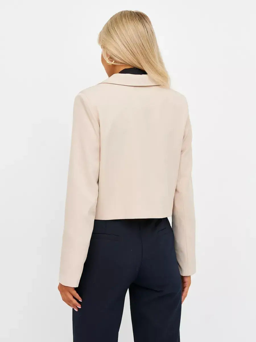 Back view of a woman wearing the Sandstone Blazer by Lauven, showcasing its cropped tailored design in soft beige.