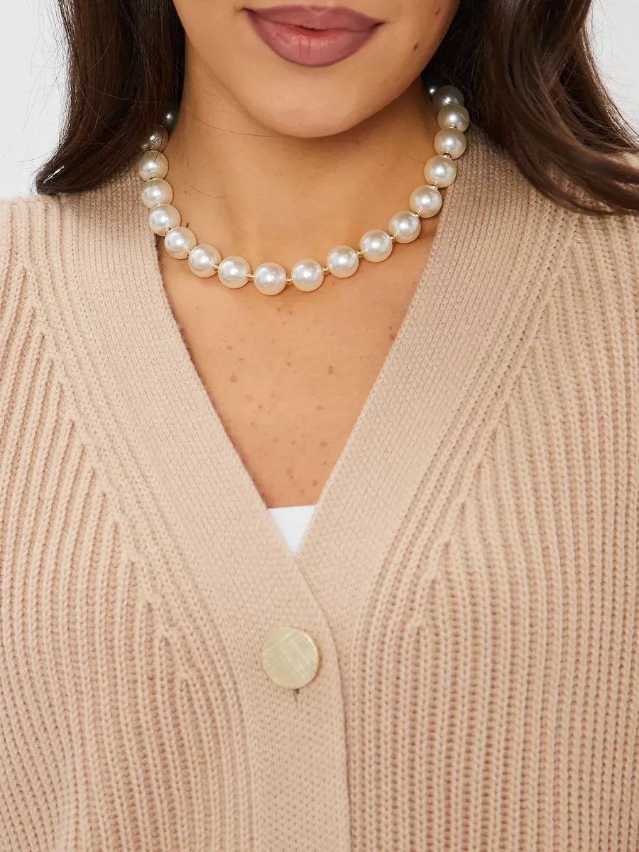 Close-up of a woman wearing a beige Sandstone Cardigan with a pearl necklace, showcasing stylish knitwear by Lauven.