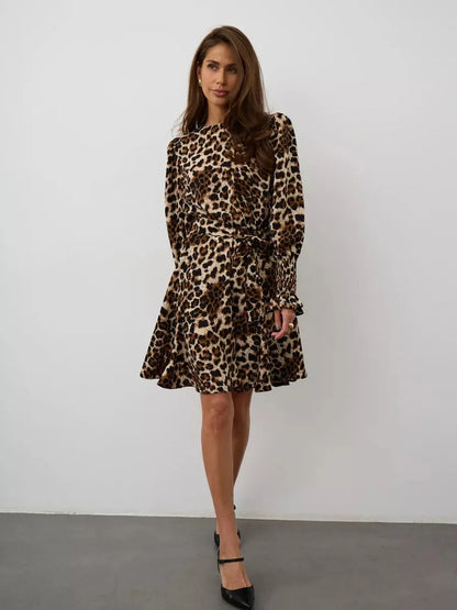 Savannah Mini Dress featuring leopard print, long sleeves, and a flattering fit with ruffle accents and a tie belt.