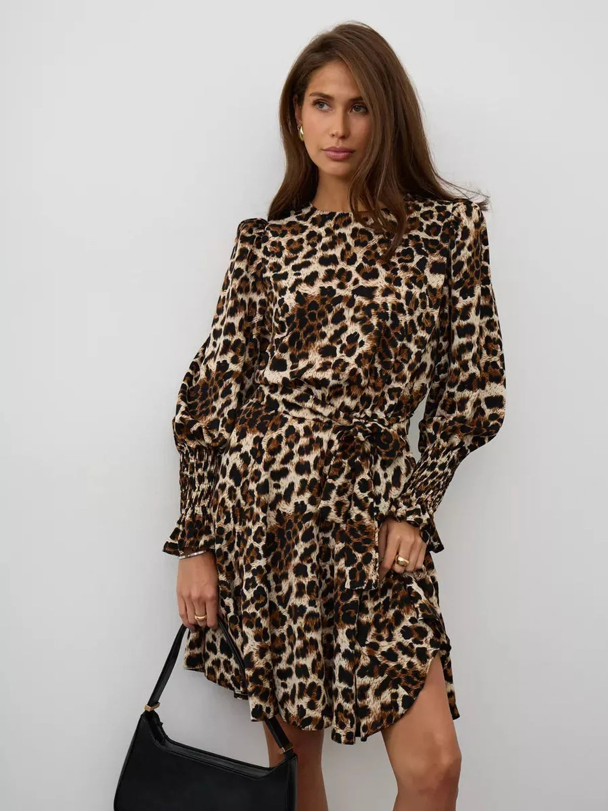 Savannah Mini Dress featuring bold leopard print, ruffle details, and a waist-defining tie, styled with a chic handbag.