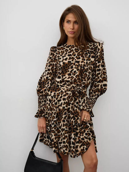Savannah Mini Dress featuring bold leopard print, ruffle details, and a waist-defining tie, styled with a chic handbag.