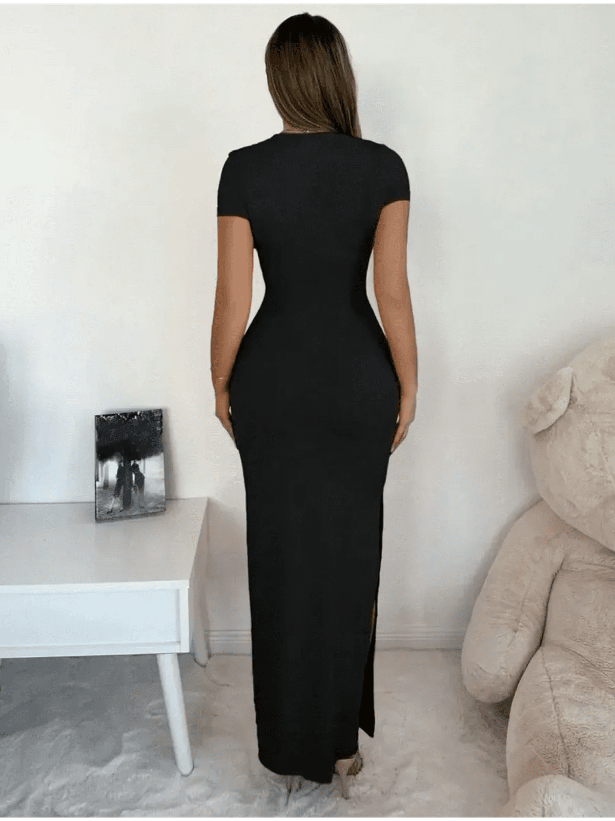 Back view of a woman in a sleek black Sculpted Elegance Maxi Dress featuring a flattering fit and subtle side slit.