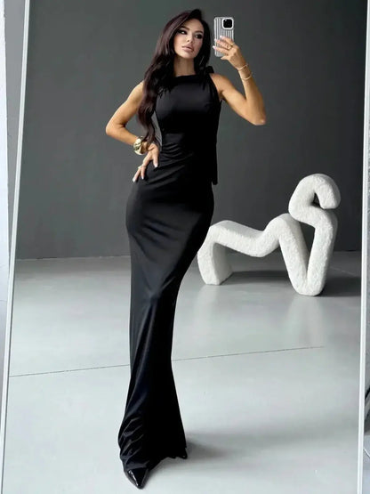 Elegant woman in Sculpted Noir Maxi Dress showcasing sleek silhouette and bow detail against a modern backdrop.