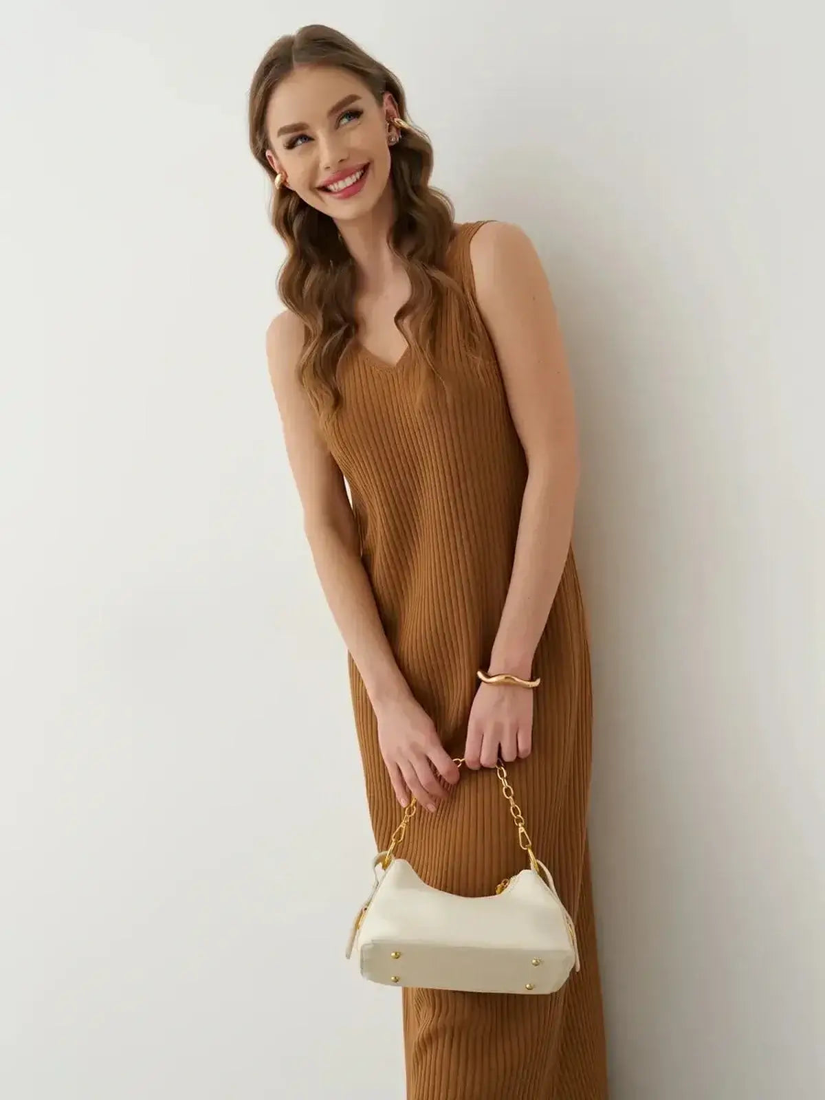Model wearing the Serena Maxi Dress in ribbed brown fabric, featuring a V-neckline and styled with a white handbag.