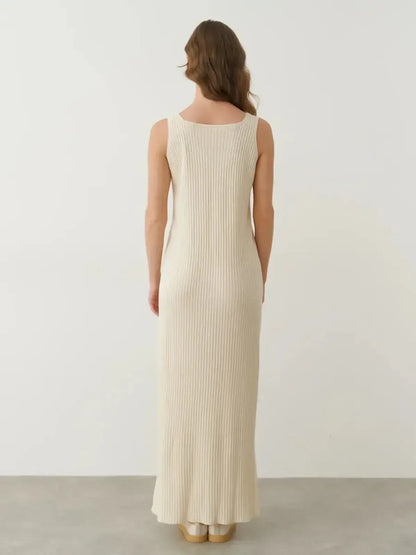 Back view of a woman in a beige Serene Rib Maxi Dress, showcasing its elegant ribbed texture and ankle-grazing silhouette.