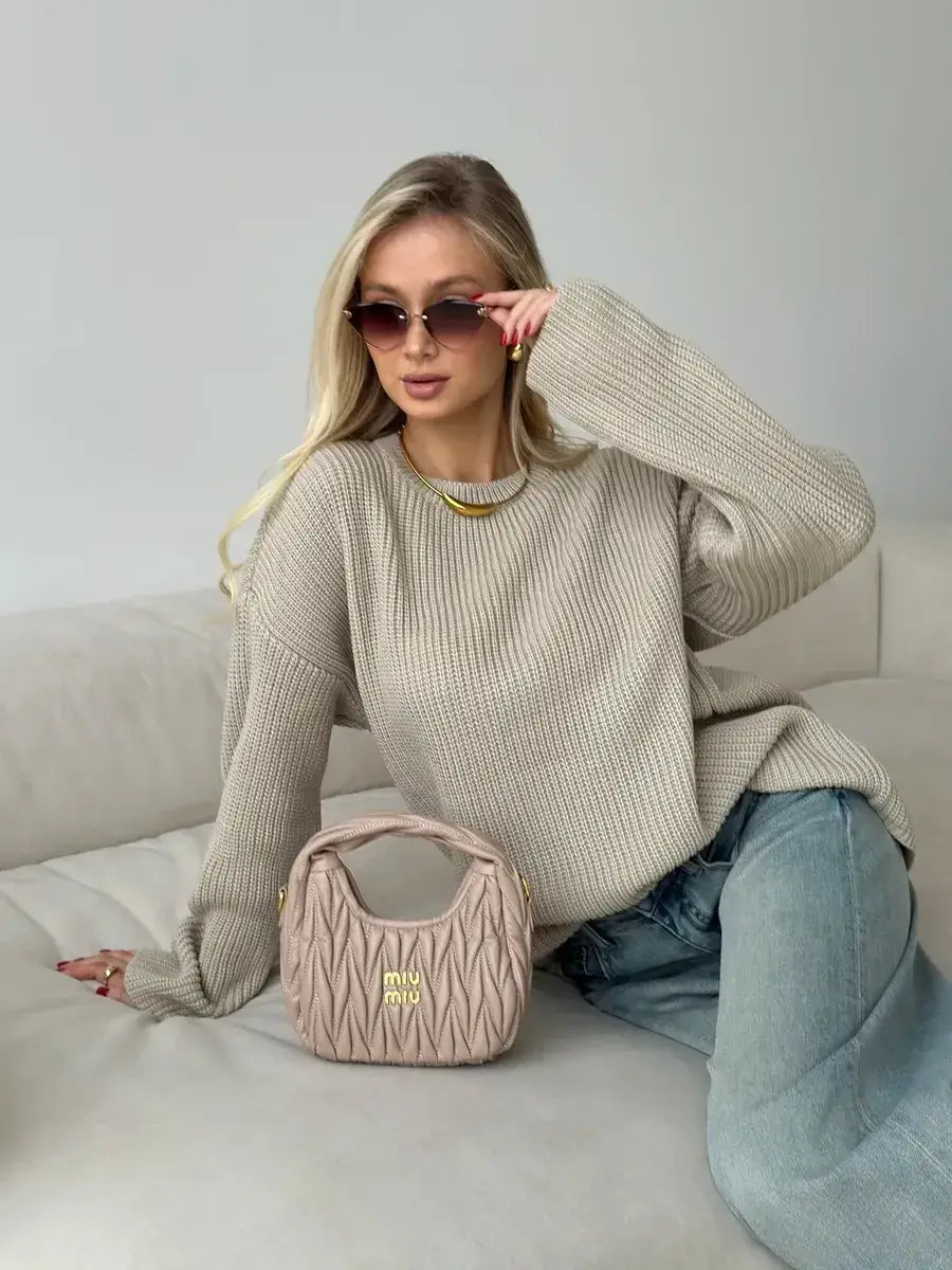Woman wearing Sierra Sweater, an oversized beige knit, paired with stylish sunglasses and a designer handbag.