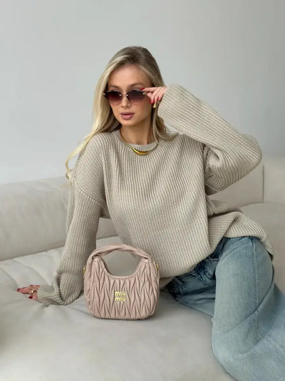 Woman wearing Sierra Sweater, an oversized beige knit, paired with stylish sunglasses and a designer handbag.