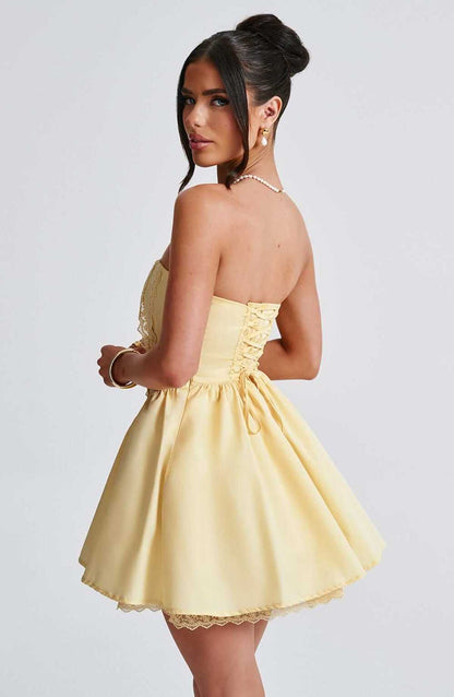 Model wearing a yellow Skye Mini Dress with corset design, showcasing a strapless neckline and playful skirt.
