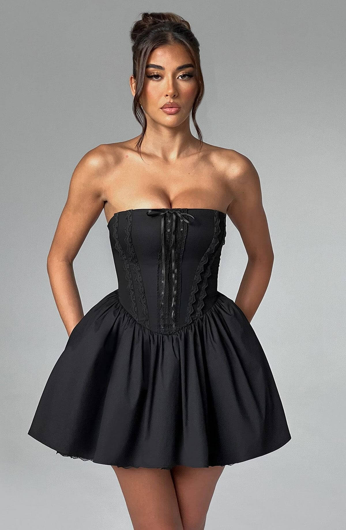 Model wearing a strapless black corset mini dress, showcasing a flared skirt and intricate detailing, perfect for parties.