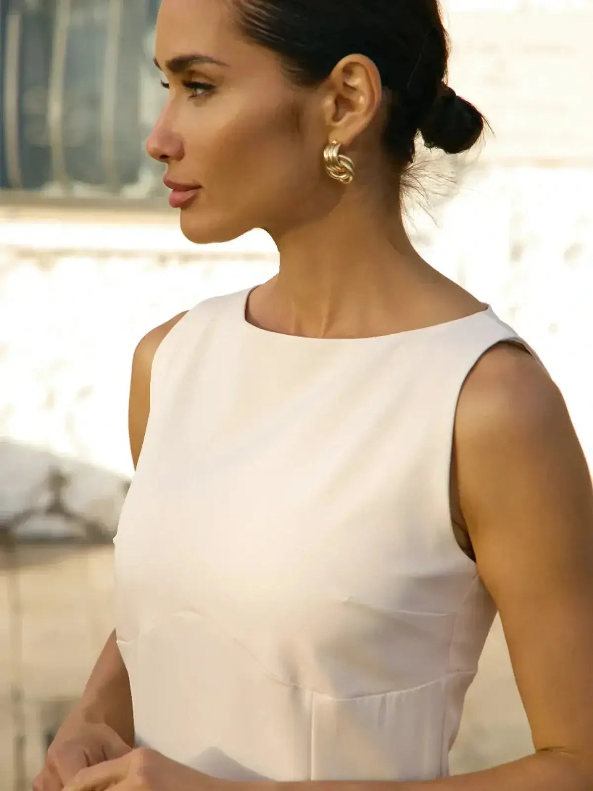 Close-up of a woman in a sleeveless white mini dress showcasing a round neckline, perfect for summer and wedding guest events.
