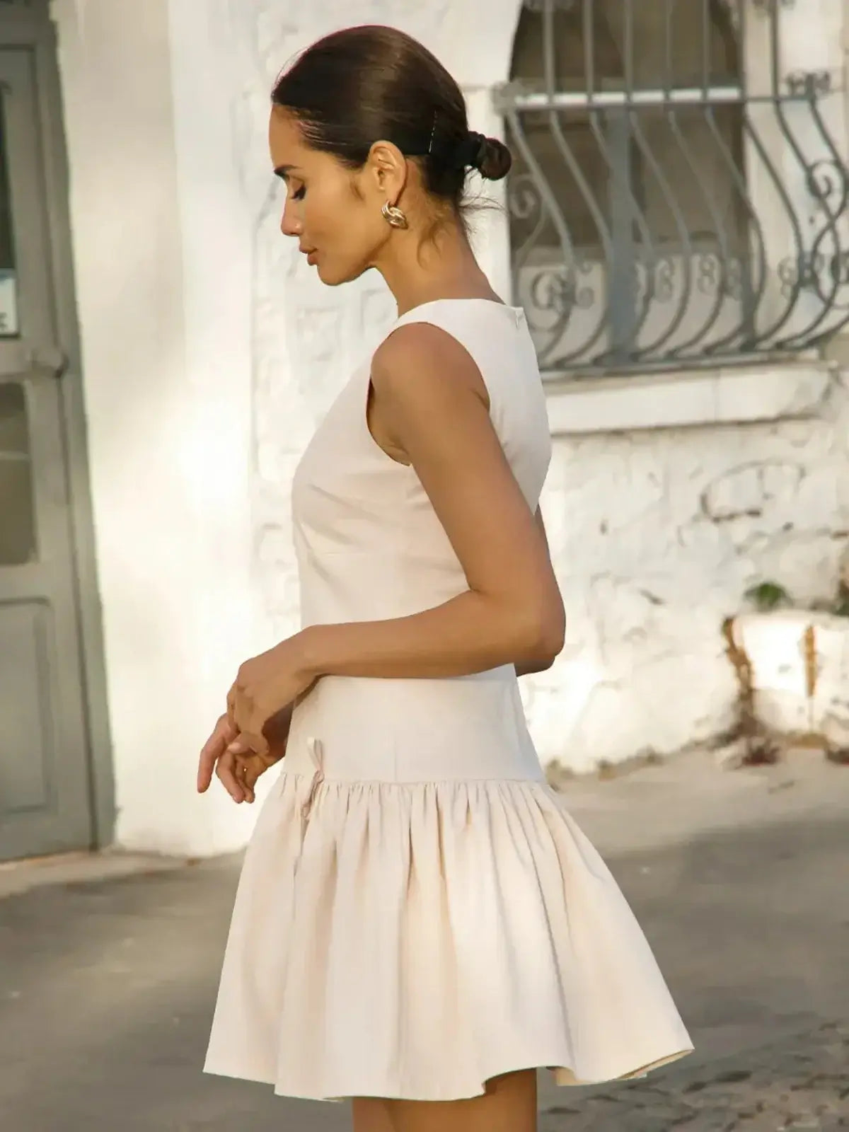Profile view of a model wearing a soft beige mini dress with a flared skirt, perfect for summer occasions.