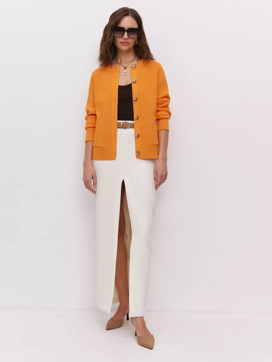 Solana Cardigan by Lauven in bold orange, styled with a sleek white skirt and sunglasses, showcasing modern elegance.