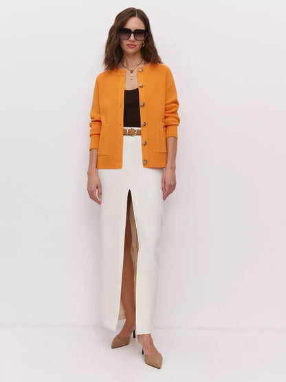 Solana Cardigan by Lauven in bold orange, styled with a sleek white skirt and sunglasses, showcasing modern elegance.