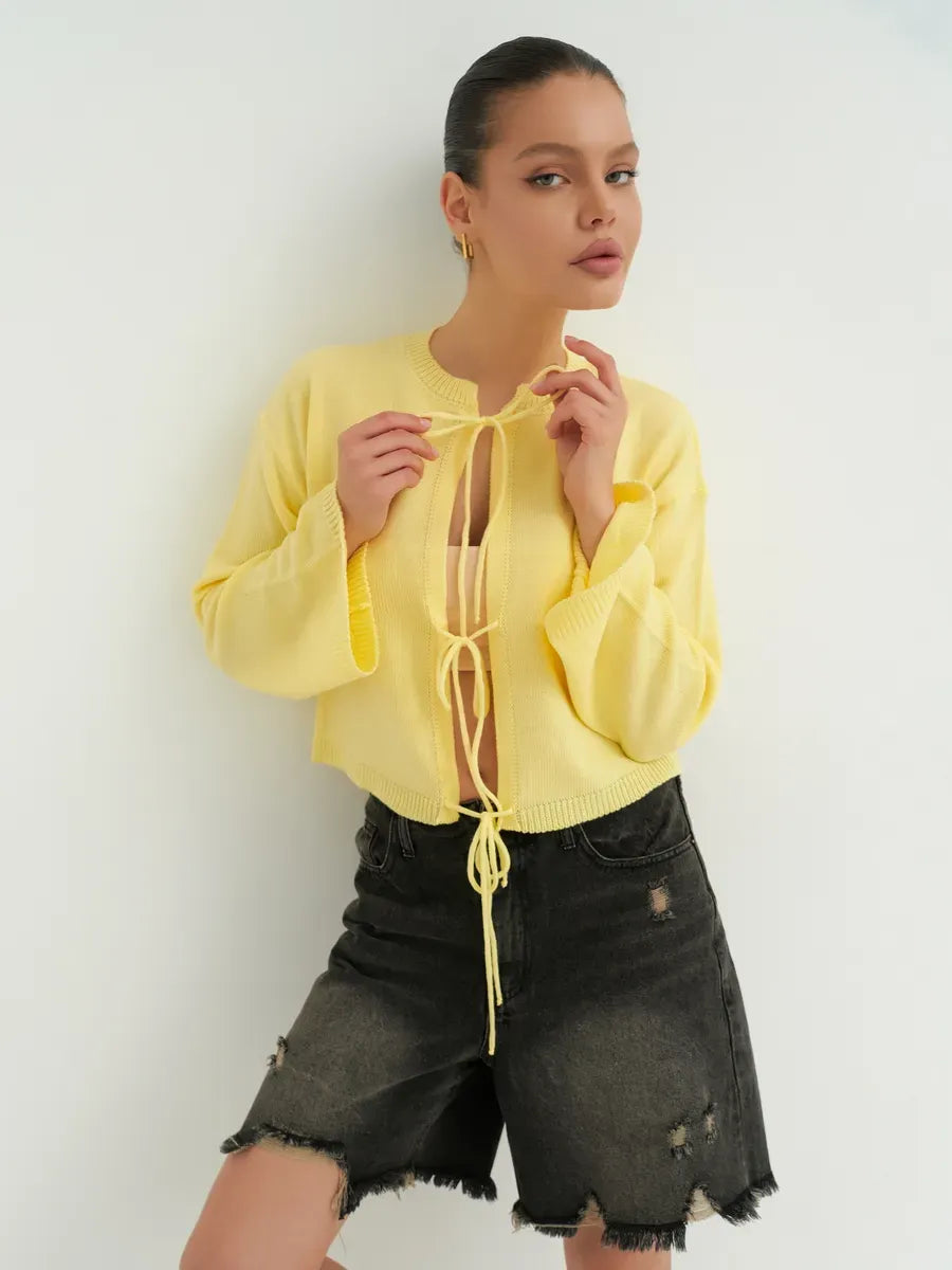 Cropped yellow Solara Cardigan by Lauven with tie-front detail, styled with black shorts for a chic summer look.